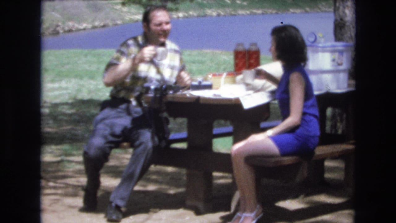 In supplied 1973 Lake Tahoe, Nevada home-movie footage, a man in a plaid shirt and a woman in a blue sleeveless dress sit across from each other at a lakeside picnic table.