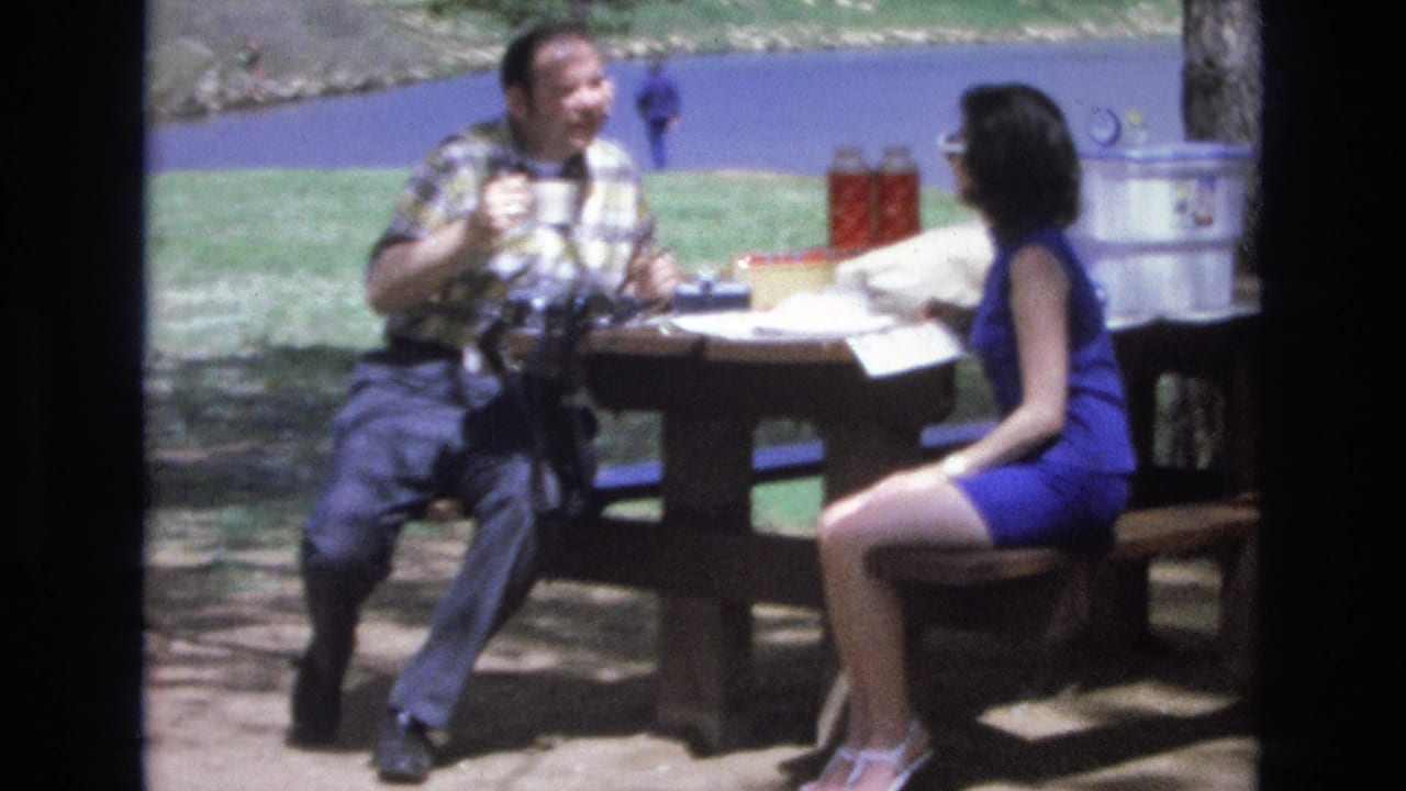 The couple faces each other at the picnic table, with cups and a cooler visible behind them.