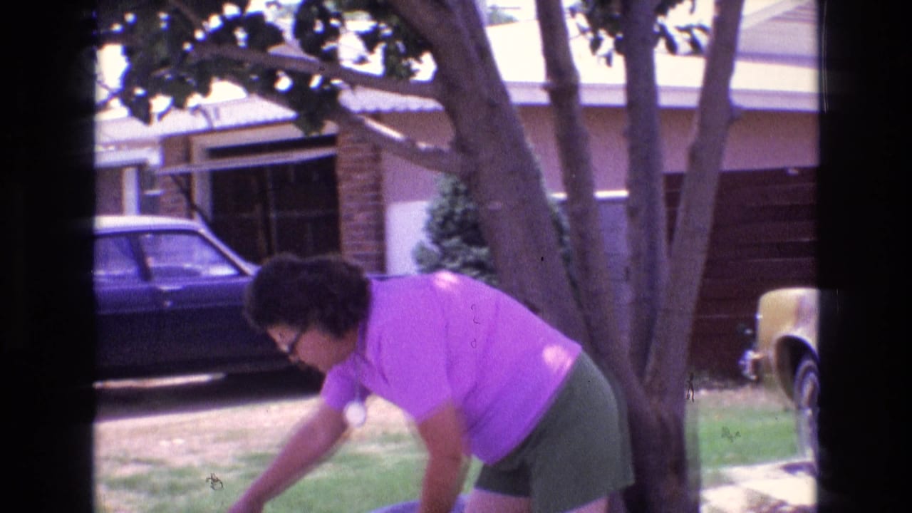 A woman in a purple shirt bends over yard work near trees, a driveway, parked cars, and a ranch-style home in the supplied 1973 New Mexico setting.