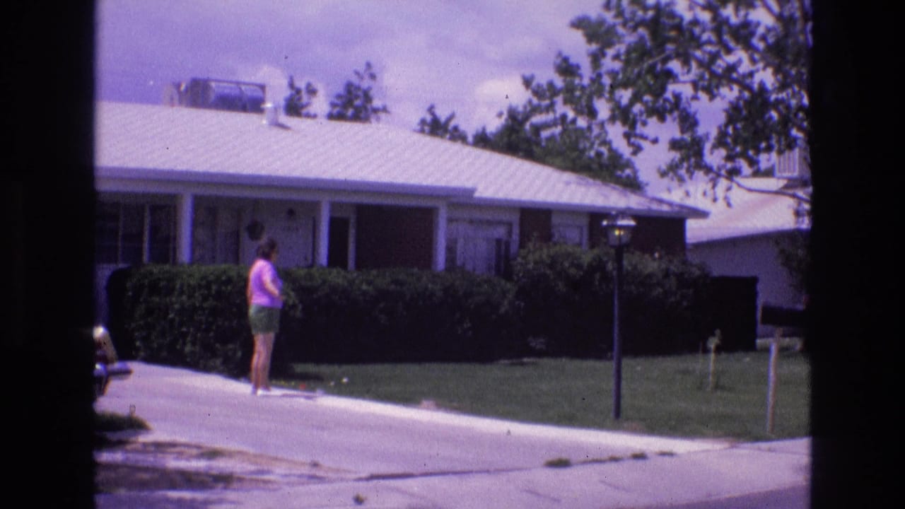 Woman walking beside a lawn and hedge in front of a single-story suburban house.