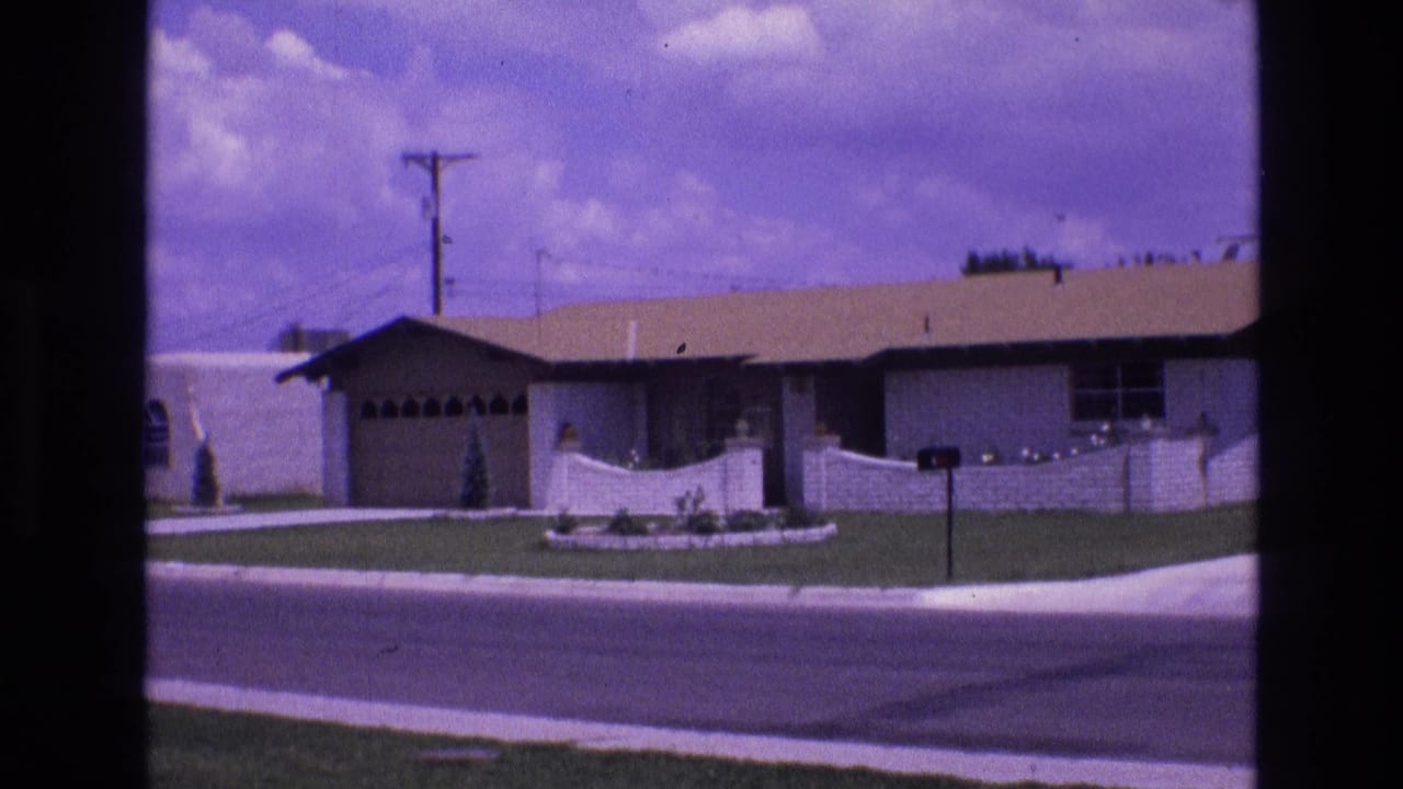 1973 New Mexico 8mm frame showing a low single-story suburban house with a front lawn, low wall, driveway, mailbox, and street in the foreground.