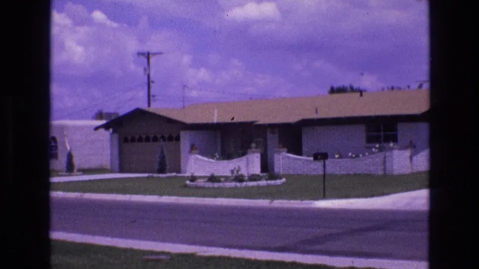 1973 New Mexico 8mm frame showing a low single-story suburban house with a front lawn, low wall, driveway, mailbox, and street in the foreground.