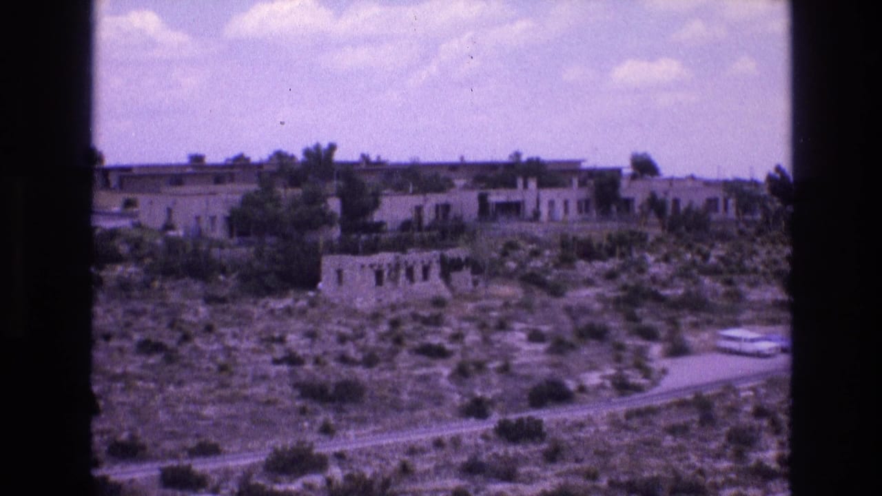 1973 New Mexico 8mm frame showing a weathered stone ruin with window openings on a scrub hillside below long low adobe-style buildings.