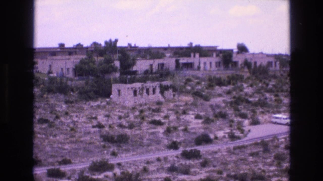 Low stucco buildings scattered across scrubby desert ground under a bright cloudy sky.
