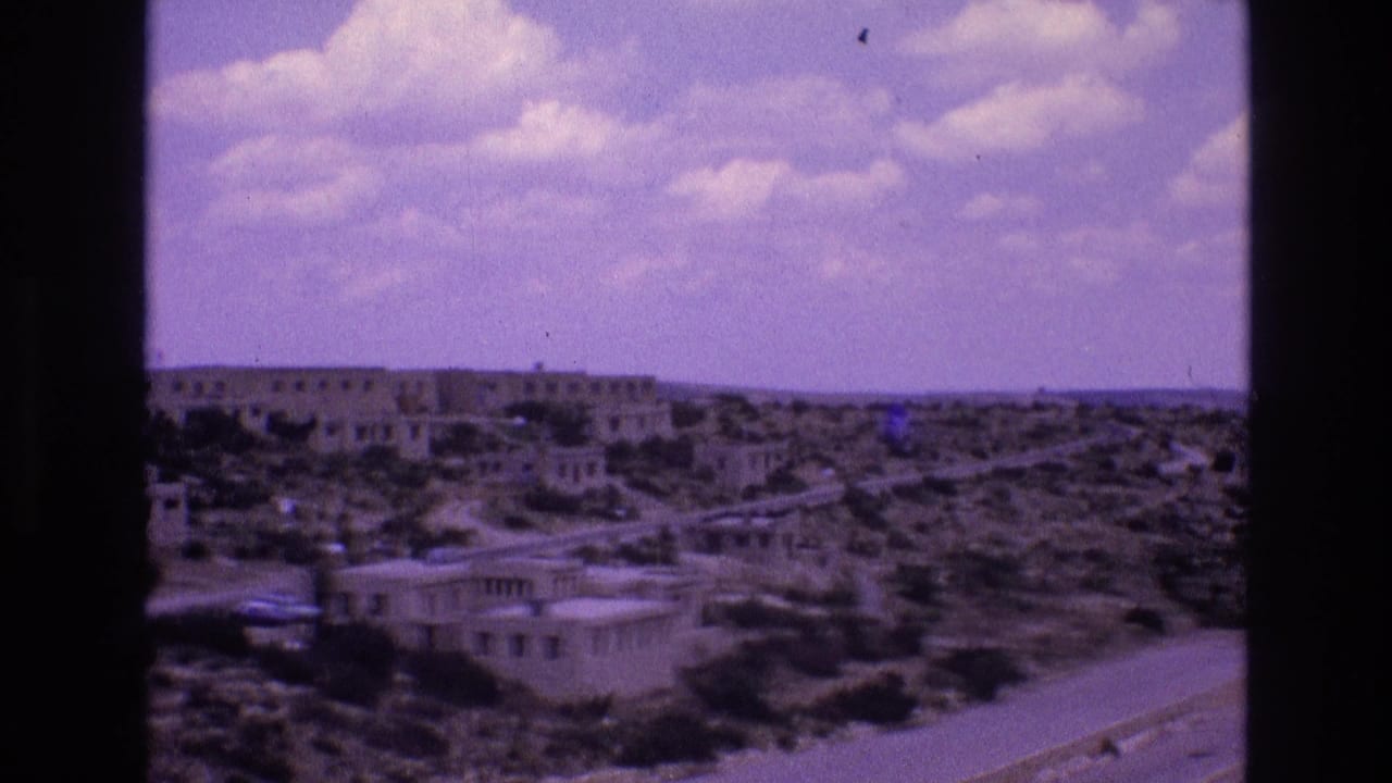 Similar wide desert view with low buildings, road, scrubland, and open sky.