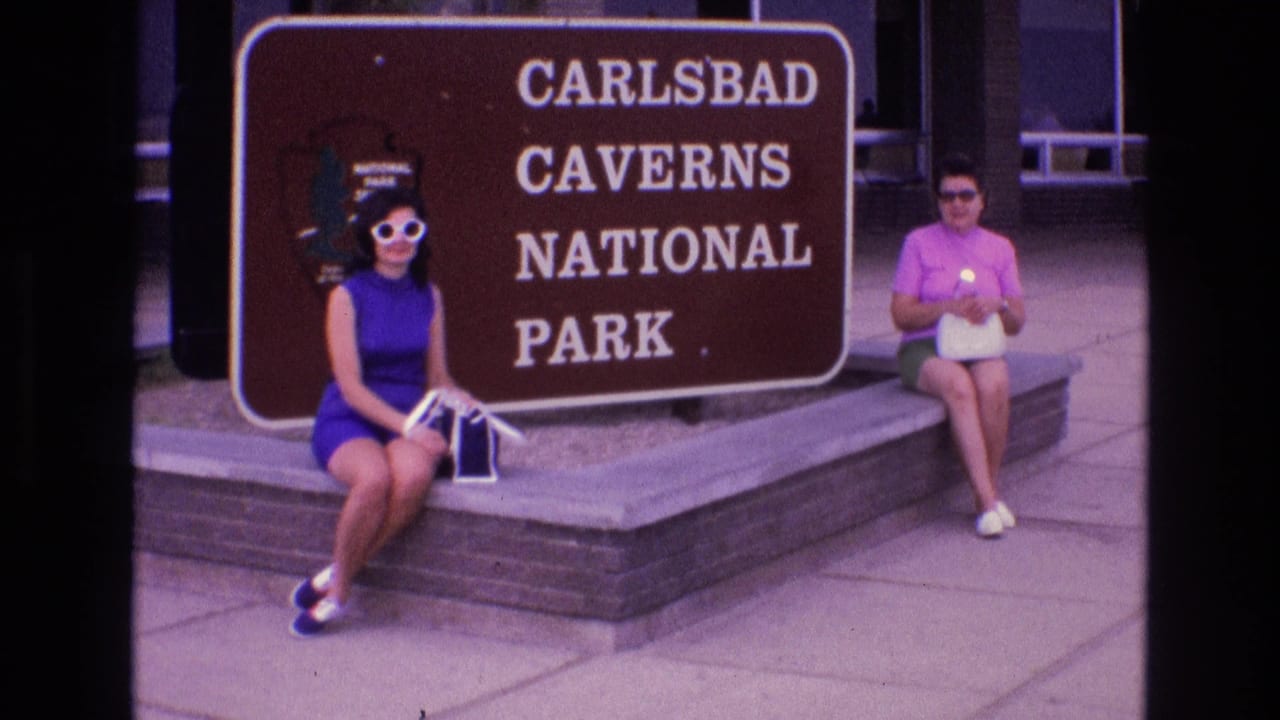 Two women remain seated near the brown national park sign.
