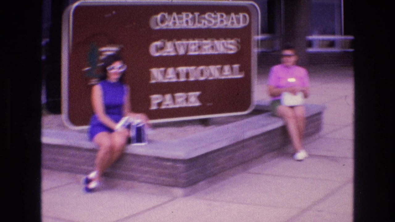 Two women remain seated beside the Carlsbad Caverns National Park sign as the frame softens.