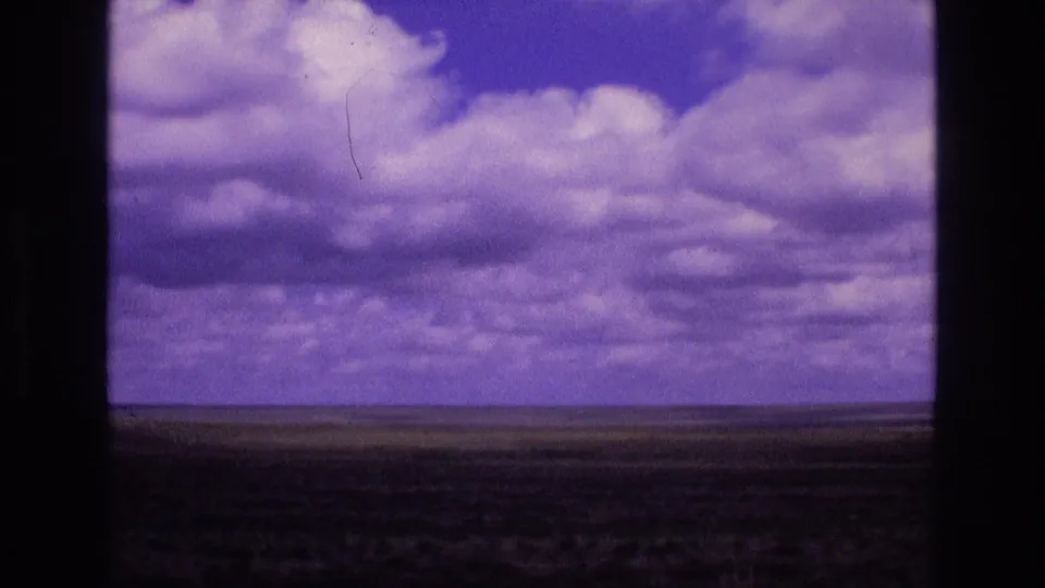 1973 New Mexico landscape frame with distant flat plains, a low horizon, layered clouds, purple color shift, and dark 8mm gate edges.