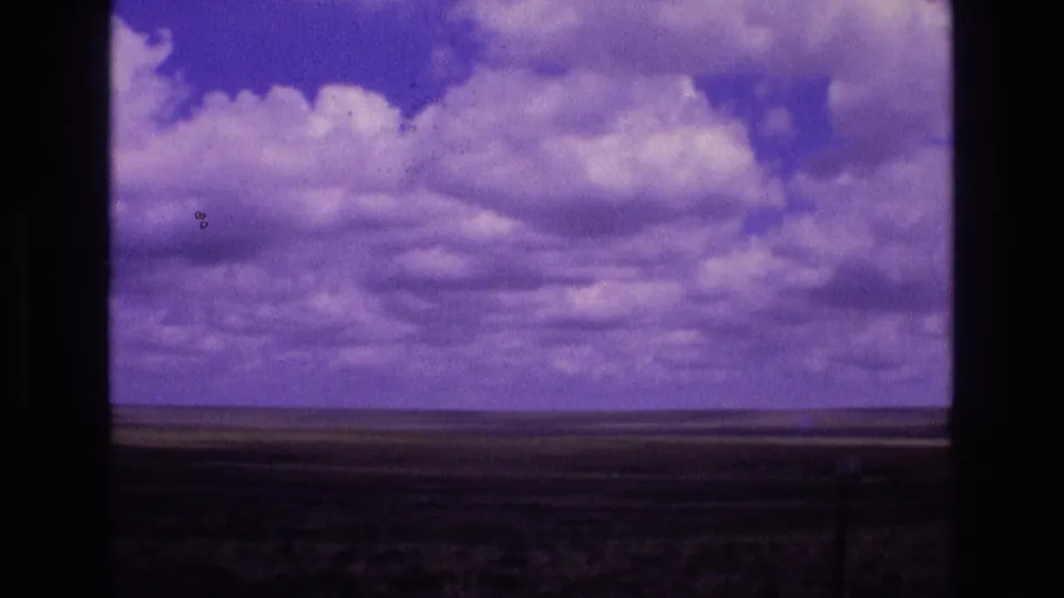 1973 New Mexico 8mm frame emphasizing a broad purple-clouded sky above a thin grassland horizon, with visible film borders and specks.
