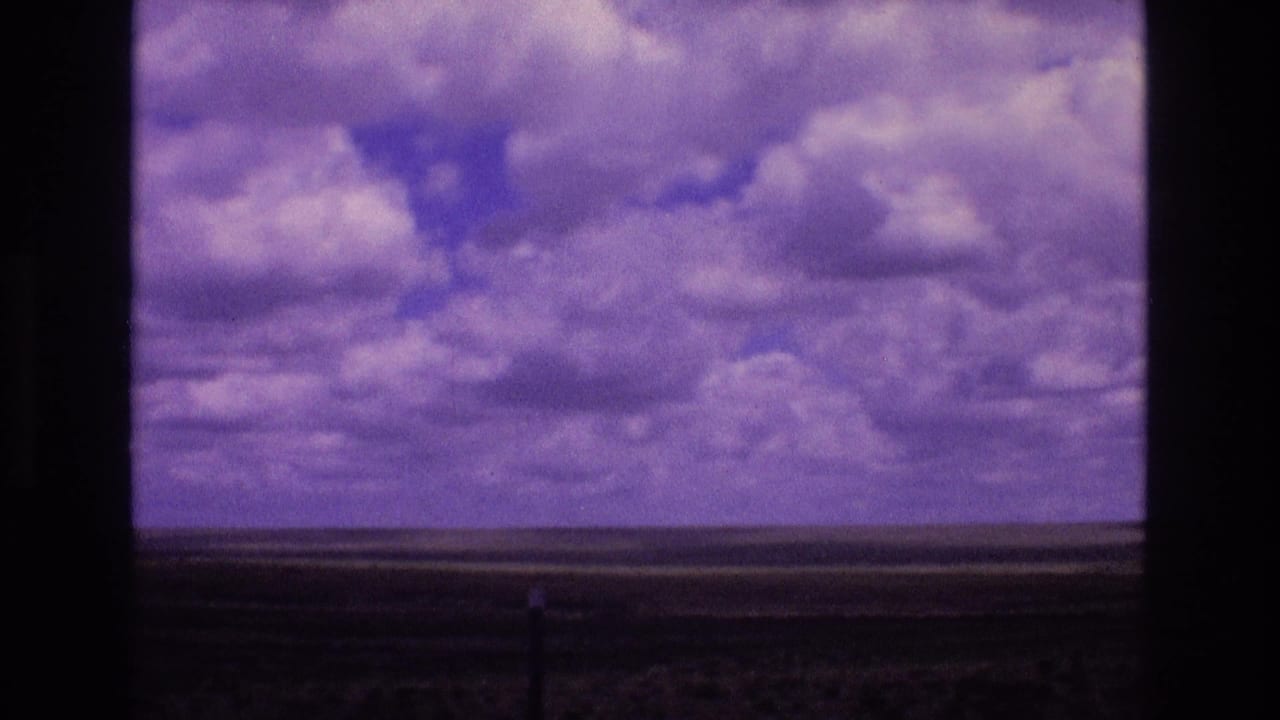 1973 New Mexico home-movie frame showing a broad cloud-filled sky and low open horizon viewed through a dark window crossbar.