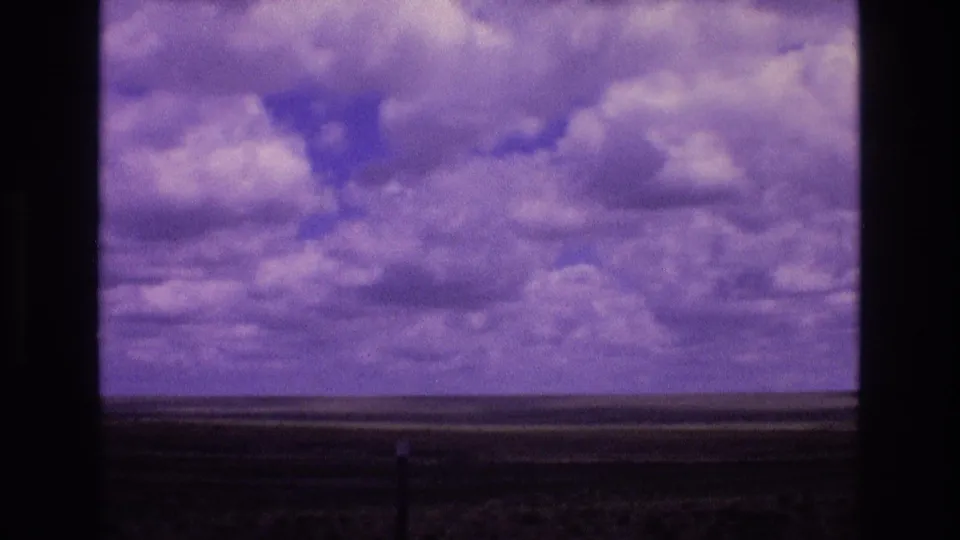 1973 New Mexico home-movie frame showing a broad cloud-filled sky and low open horizon viewed through a dark window crossbar.