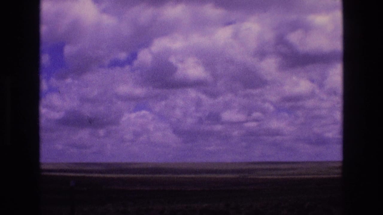 Aged 8mm view of New Mexico sky and open land, with a central dark window frame dividing the clouded horizon.