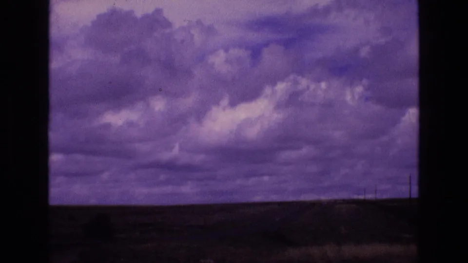 Home-movie frame of a darker cloud bank above a flat New Mexico horizon, partially obscured by the window structure in the foreground.