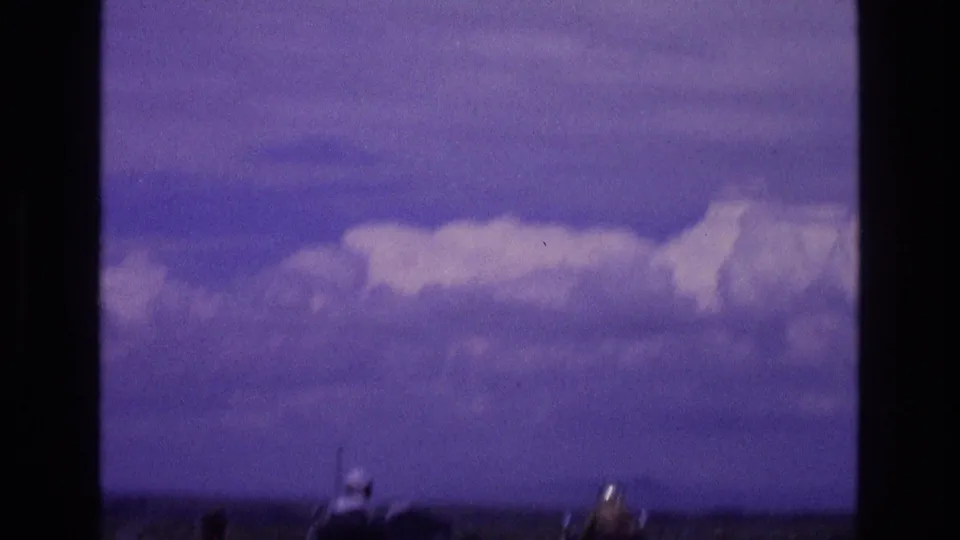 Late-frame 1973 New Mexico 8mm view of a soft purple cloud bank over a distant desert horizon, with indistinct blurred shapes entering the lower edge of the frame.