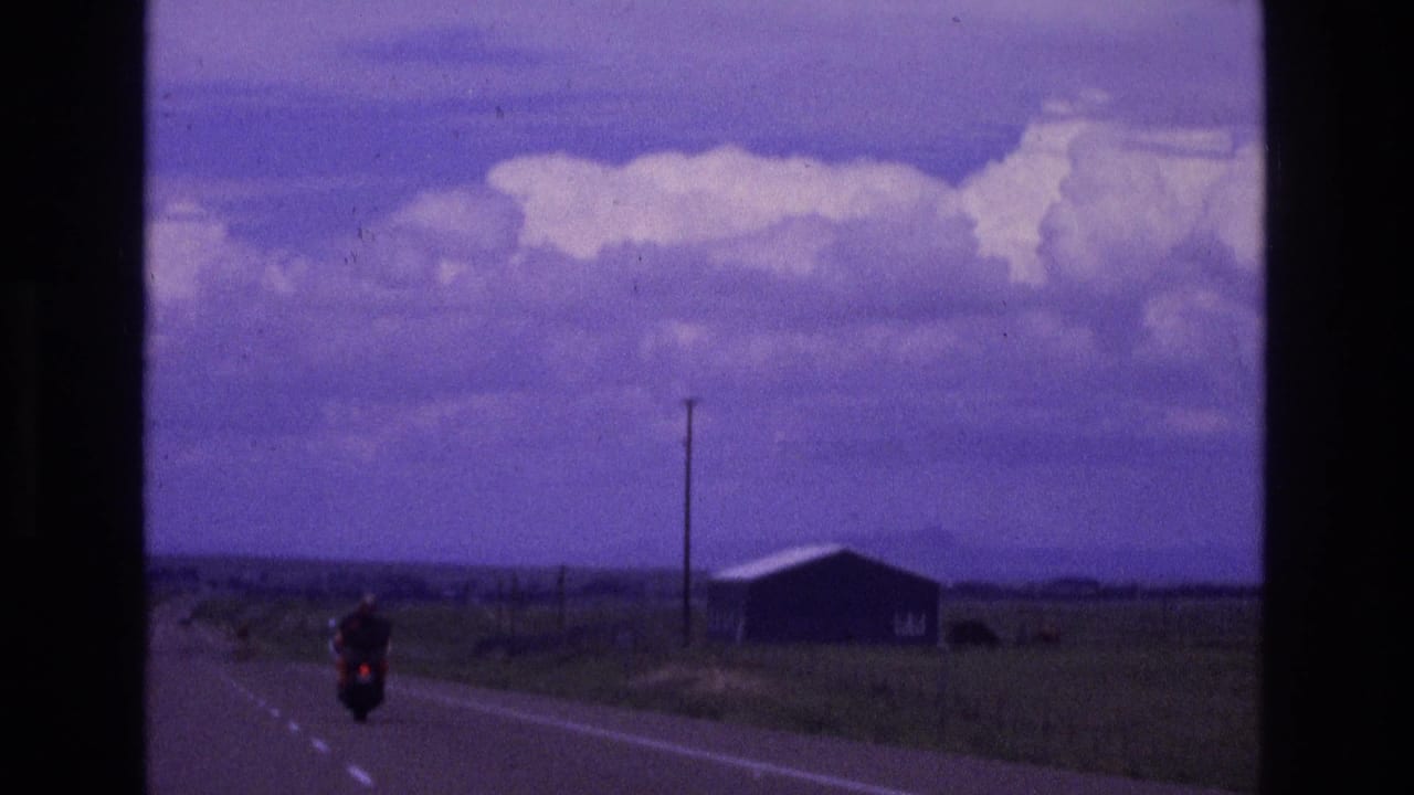 Motorcyclist riding on a rural two-lane road under a purple-tinged sky.