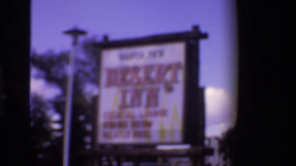 The Desert Inn sign appears in soft focus, with the large lettering and service text blurred but still recognizable against sky, trees, and roadside surroundings.