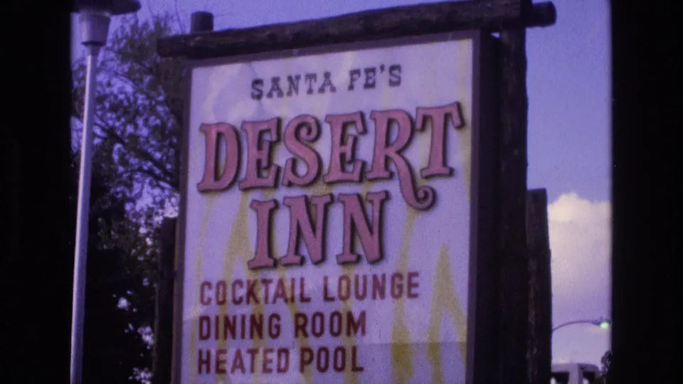 1973 8mm frame from Santa Fe showing the Desert Inn sign filling the view, with cocktail lounge, dining room, and heated pool text visible beside a street lamp and trees.
