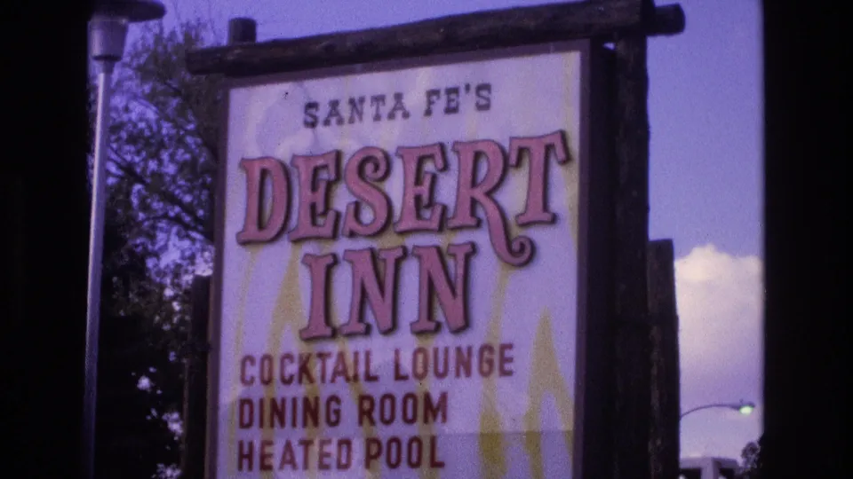 Close 1973 New Mexico 8mm view of the Santa Fe's Desert Inn sign, showing large pink lettering and listings for cocktail lounge, dining room, and heated pool.