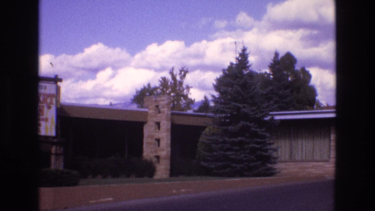 Motel exterior with stone pillar, trees, and partial sign at the left edge.