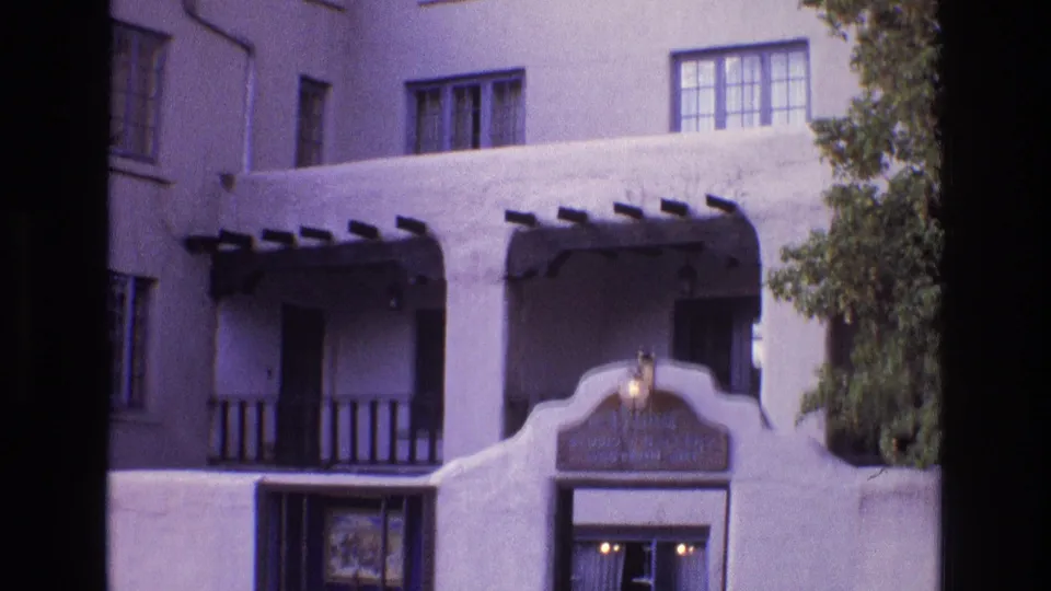 1973 New Mexico 8mm frame reframed lower on the building, showing balcony railings, dark beams, the curved top of the entrance, a small lower window, and a lit sign area.