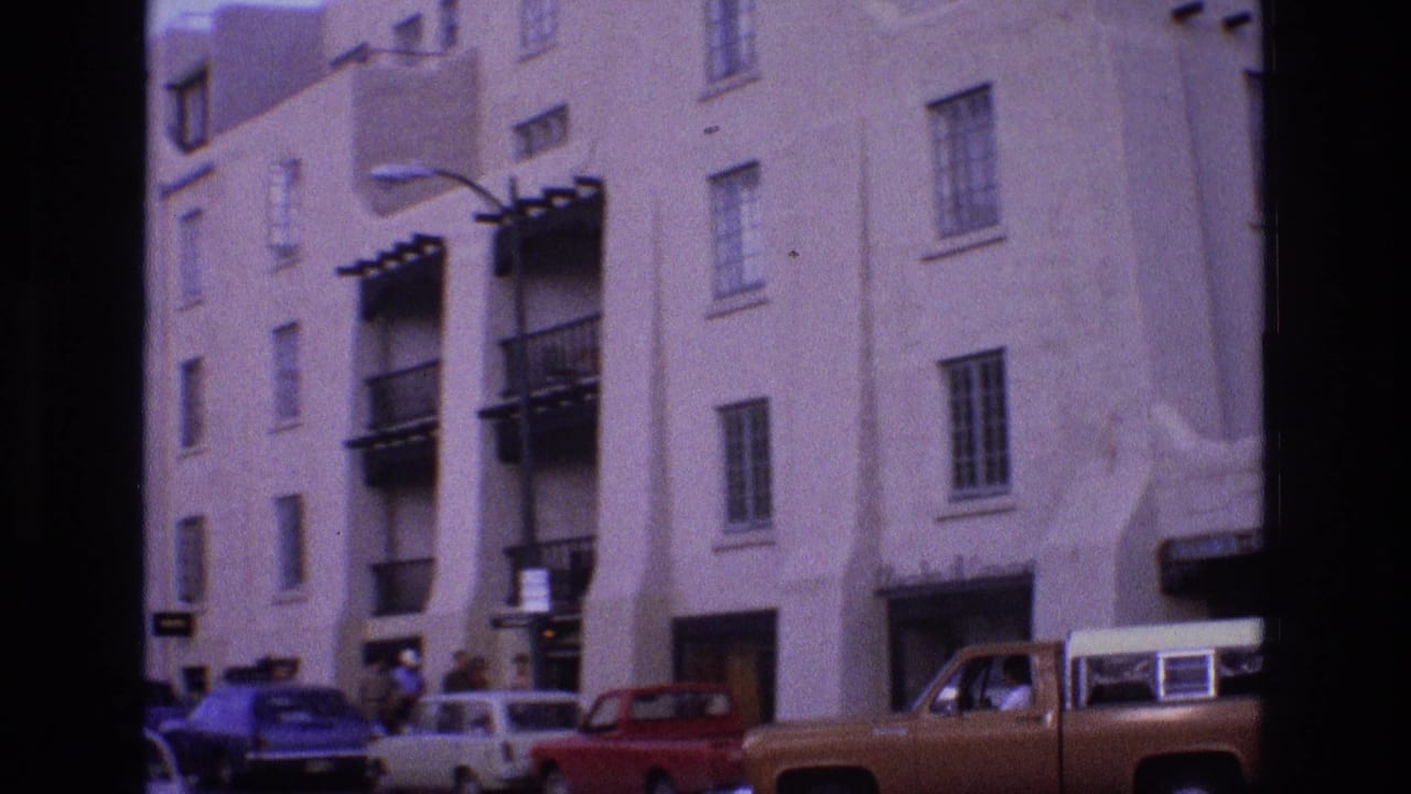 Multi-story stucco street buildings with parked cars and a brown pickup truck.