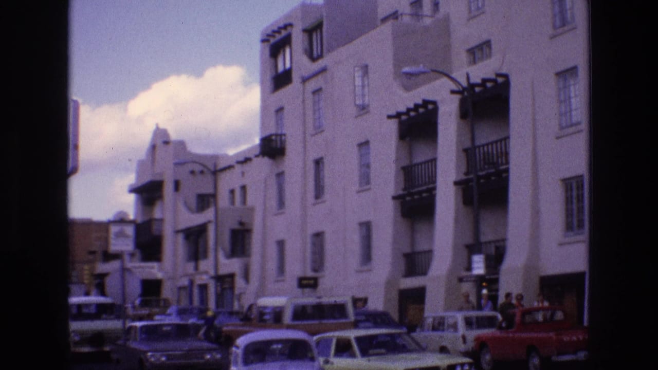 White stucco building with balconies above a busy street of older cars.