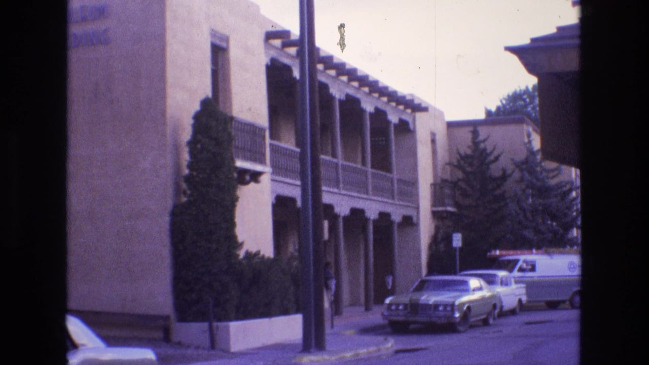 Stucco building with wooden balcony and parked cars along a quiet street.
