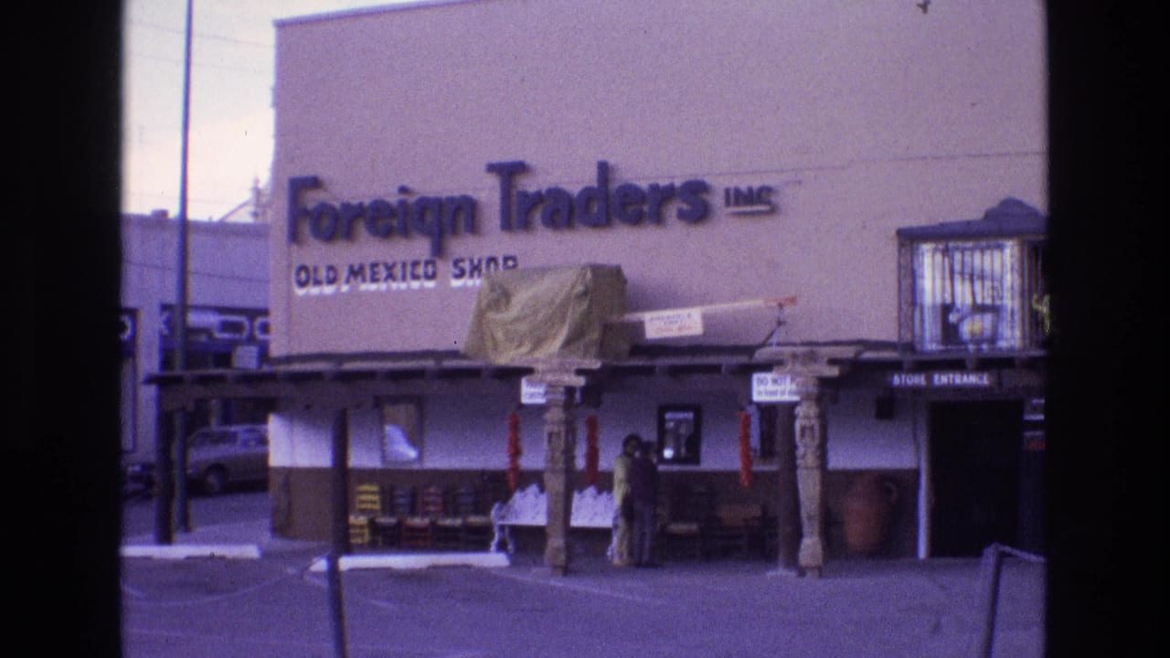 1973 New Mexico home-movie frame of the Foreign Traders Inc. Old Mexico Shop facade, showing the large wall sign, shaded entrance, decorative posts, outdoor displays, and two people standing near the doorway.