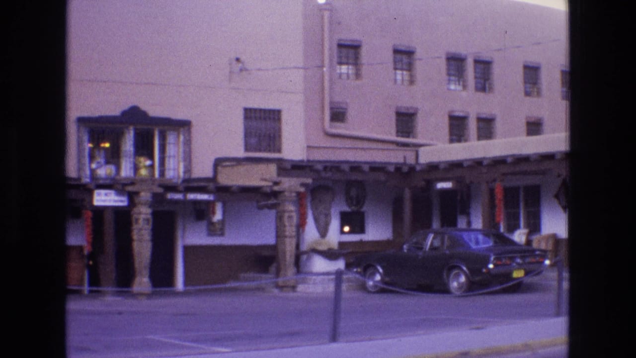 1973 New Mexico exterior view of a Southwestern-style commercial building, signage, display objects, and a black sedan parked curbside.