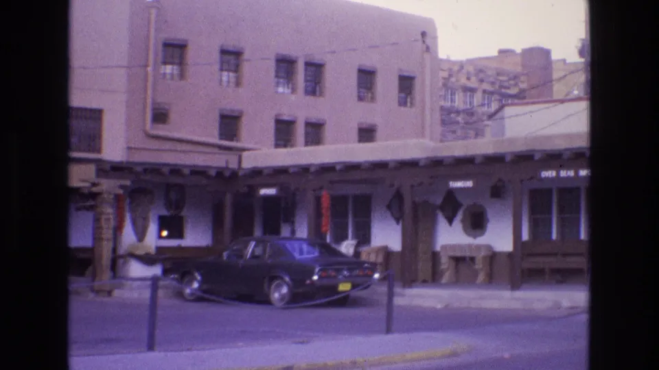 End frame of the 1973 New Mexico street view, showing the parked sedan, storefront signs, covered walkway, and Southwestern architectural details.