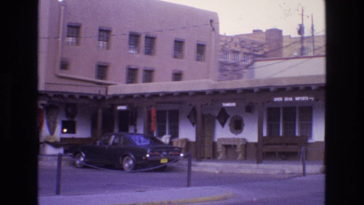 Street view of a low storefront with a dark car parked at the curb.