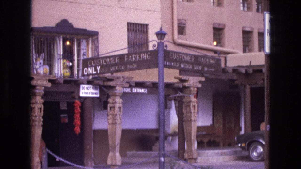 Storefront entrance with customer parking signs, carved posts, and a parked dark car on the right.