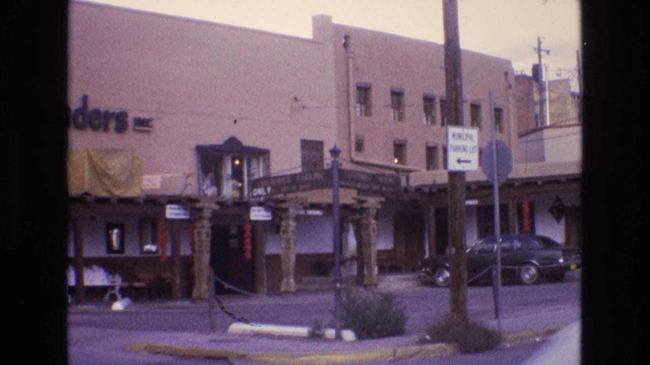 Street view of a storefront entrance, carved posts, municipal parking sign, and dark car near the curb.