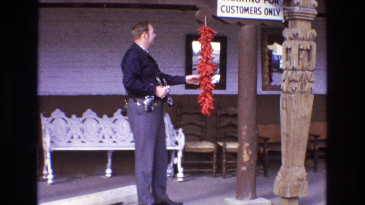 Police officer stands on a porch beside a hanging red chile pepper string.