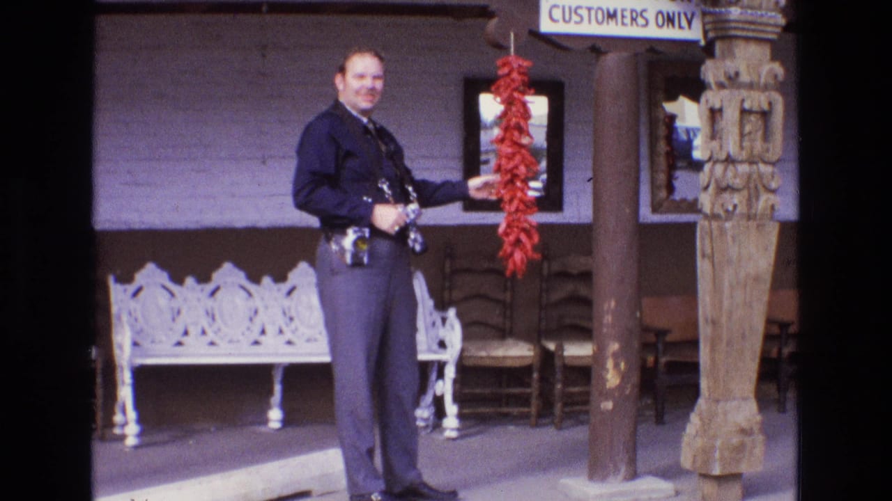 Uniformed man holding red chili peppers outside a business entrance with seating and a customer parking sign.