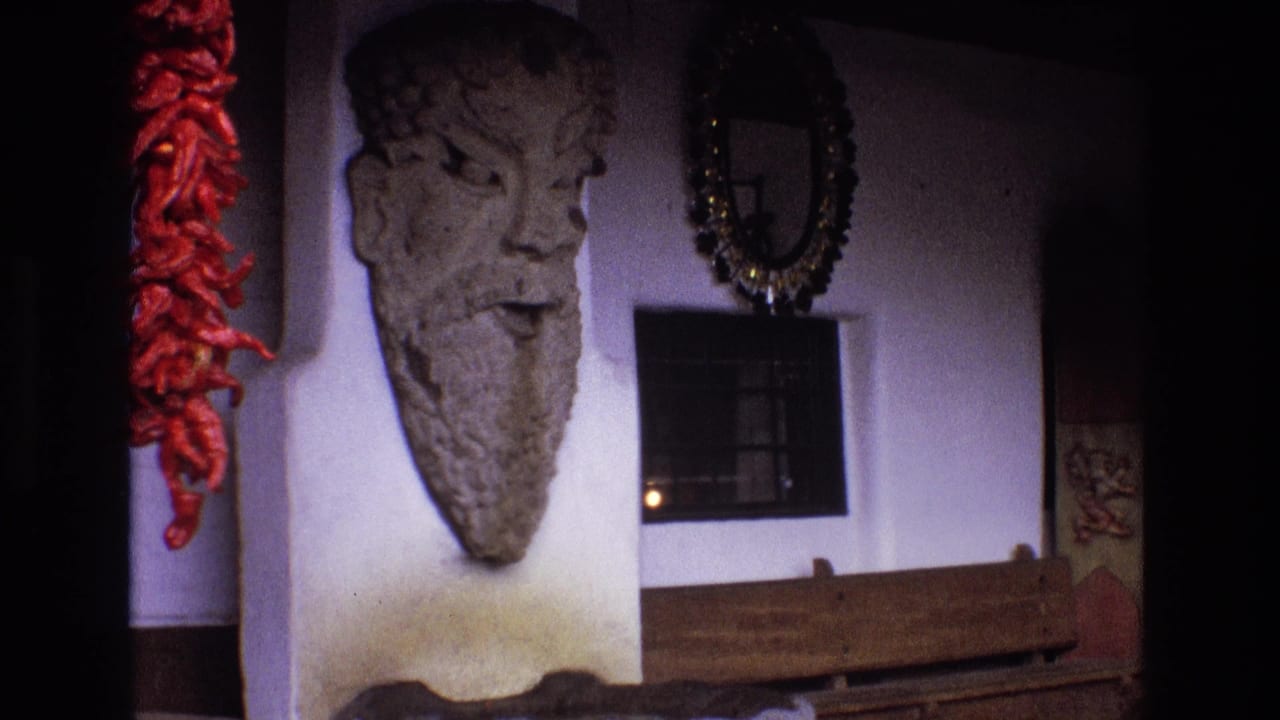 Stone face wall sculpture, red chiles, mirror, barred window, and wooden rail.