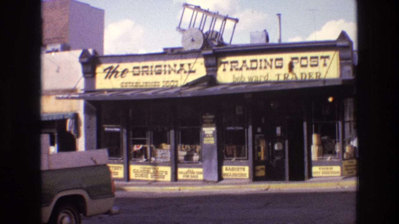 Street view of a trading post storefront seen past a dark interior edge and a parked pickup.