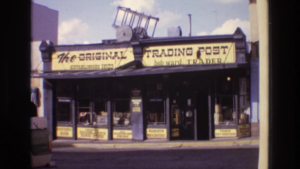 1973 New Mexico 8mm frame of the trading post facade, showing painted commercial signage, window displays, a central doorway, and roadside storefront architecture.