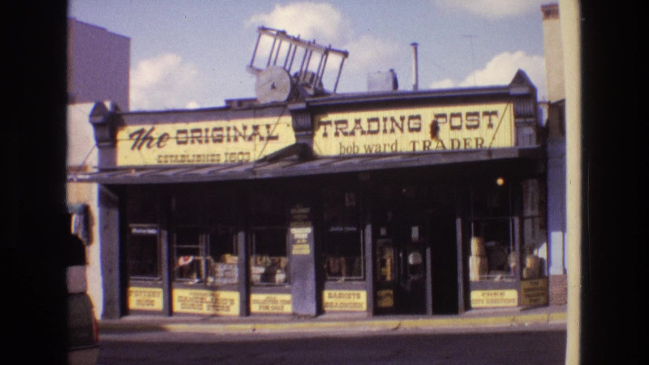 1973 New Mexico 8mm frame showing The Original Trading Post storefront with yellow signage, dark trim, sidewalk windows, and a ladder on the roofline.
