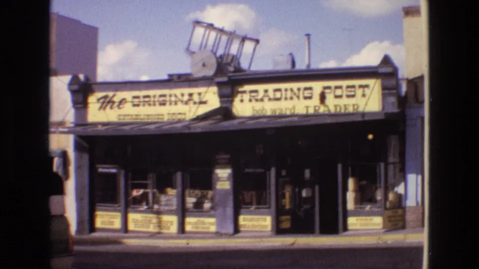 1973 New Mexico 8mm frame with the trading post sign filling the upper storefront, shaded entrance below, and display windows along the sidewalk.