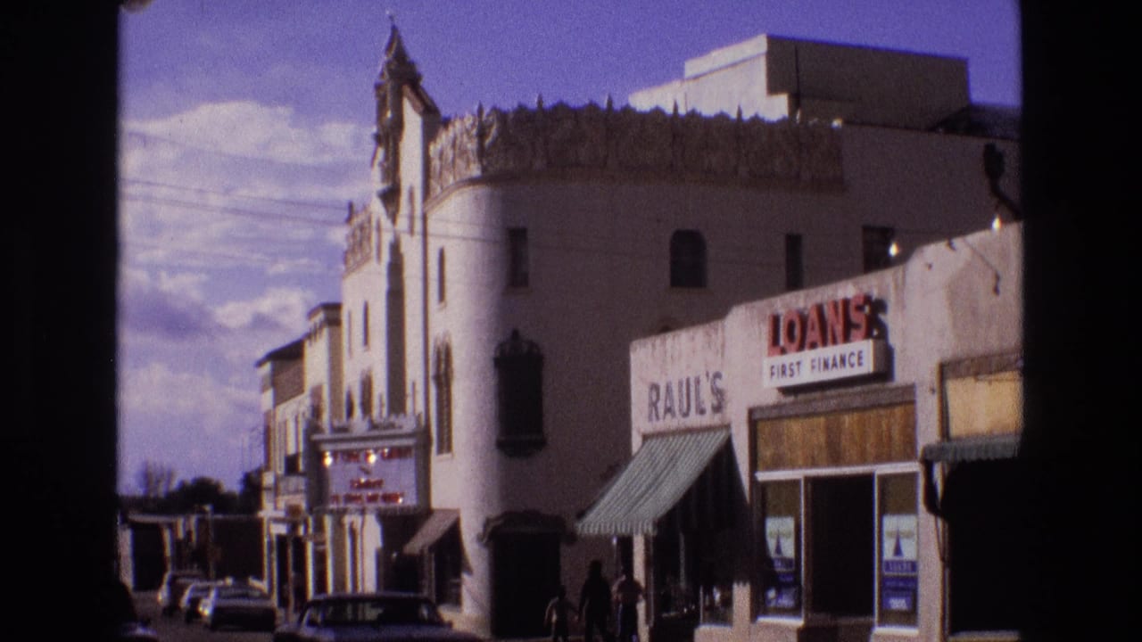 Street view of the same white building and storefronts with people near the sidewalk.