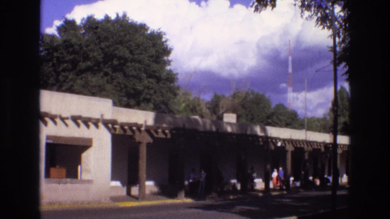 Low shaded building beside a sunny park with trees and several distant people.
