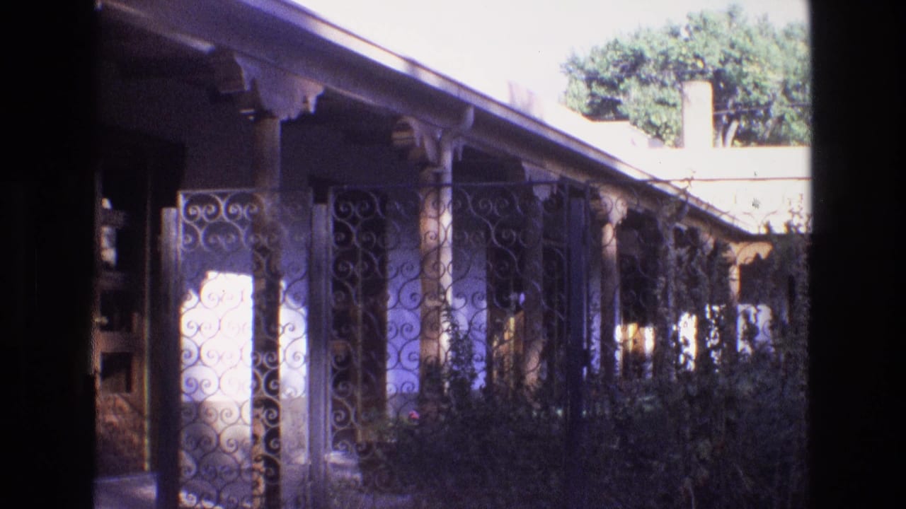 1973 New Mexico home-movie frame of a resort courtyard walkway with decorative wrought iron, shaded columns, shrubs, and bright exterior light.