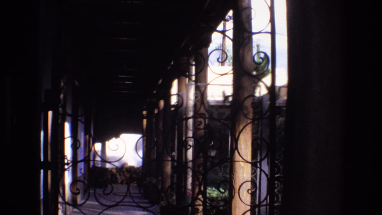 1973 New Mexico 8mm frame showing a dim covered porch with decorative wrought iron scrollwork and a bright outdoor area beyond.
