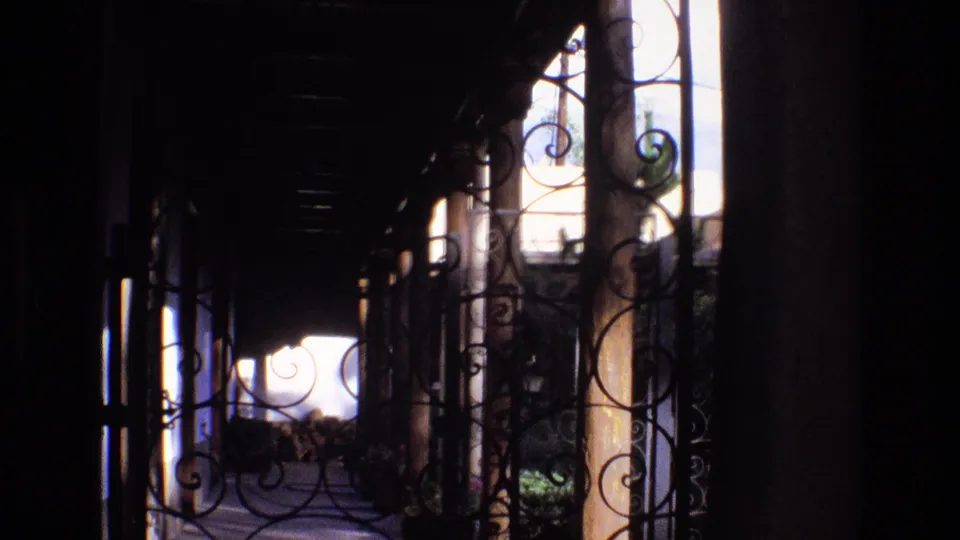 1973 New Mexico 8mm frame showing a dim covered porch with decorative wrought iron scrollwork and a bright outdoor area beyond.