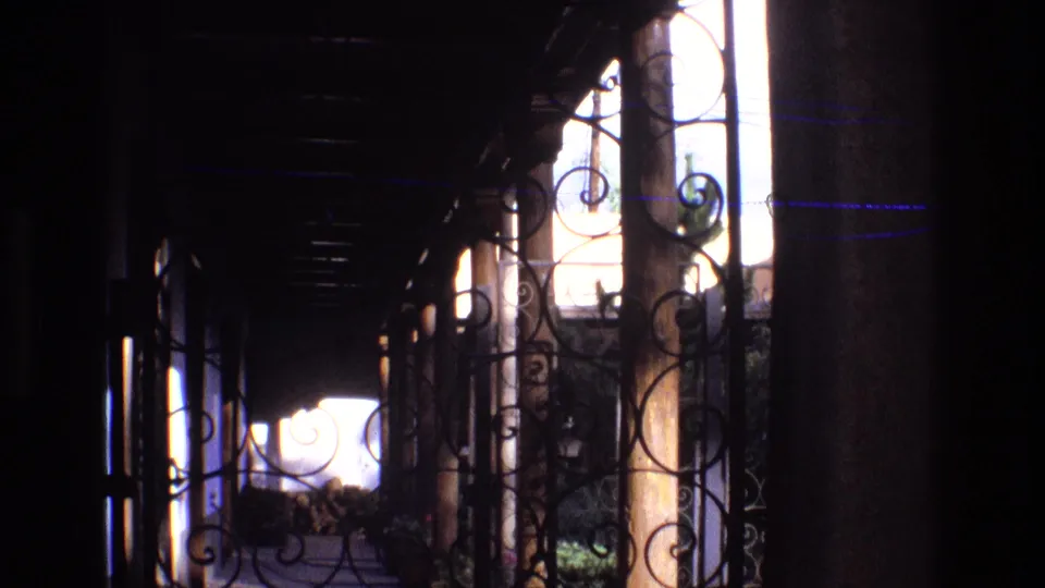 Final 1973 New Mexico porch frame with wrought iron scrollwork, dark structural posts, and a bright exterior area seen from under cover.