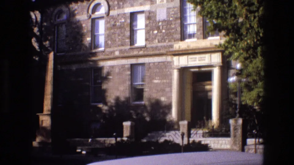 1973 New Mexico 8mm frame showing a historic-looking stone building exterior with a recessed classical entrance, arched windows, globe lamps, and tree shadows across the facade.