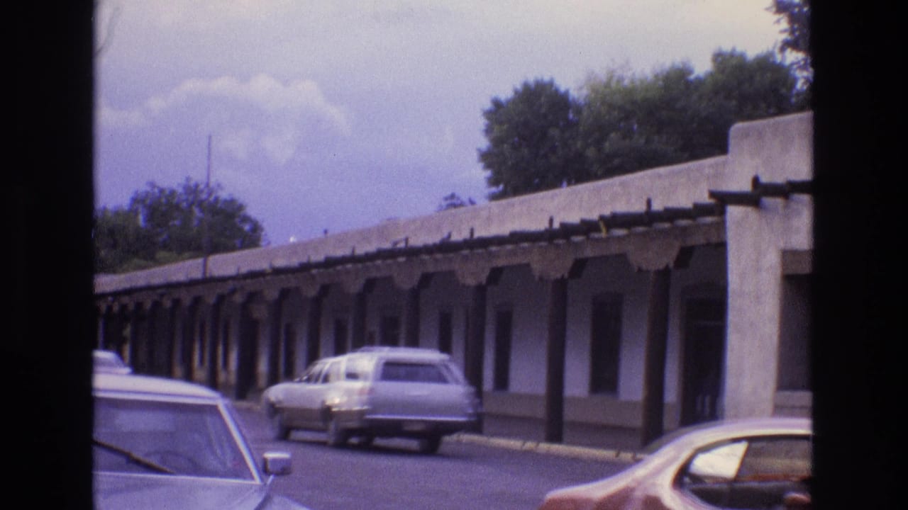 Covered walkway beside a street with a white station wagon and parked cars.