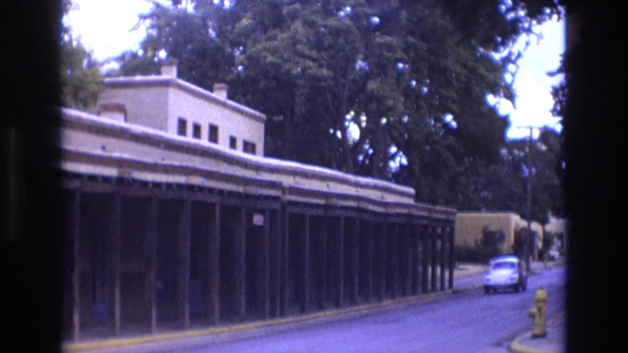 White Volkswagen Beetle approaching along the street beside the adobe-style building.