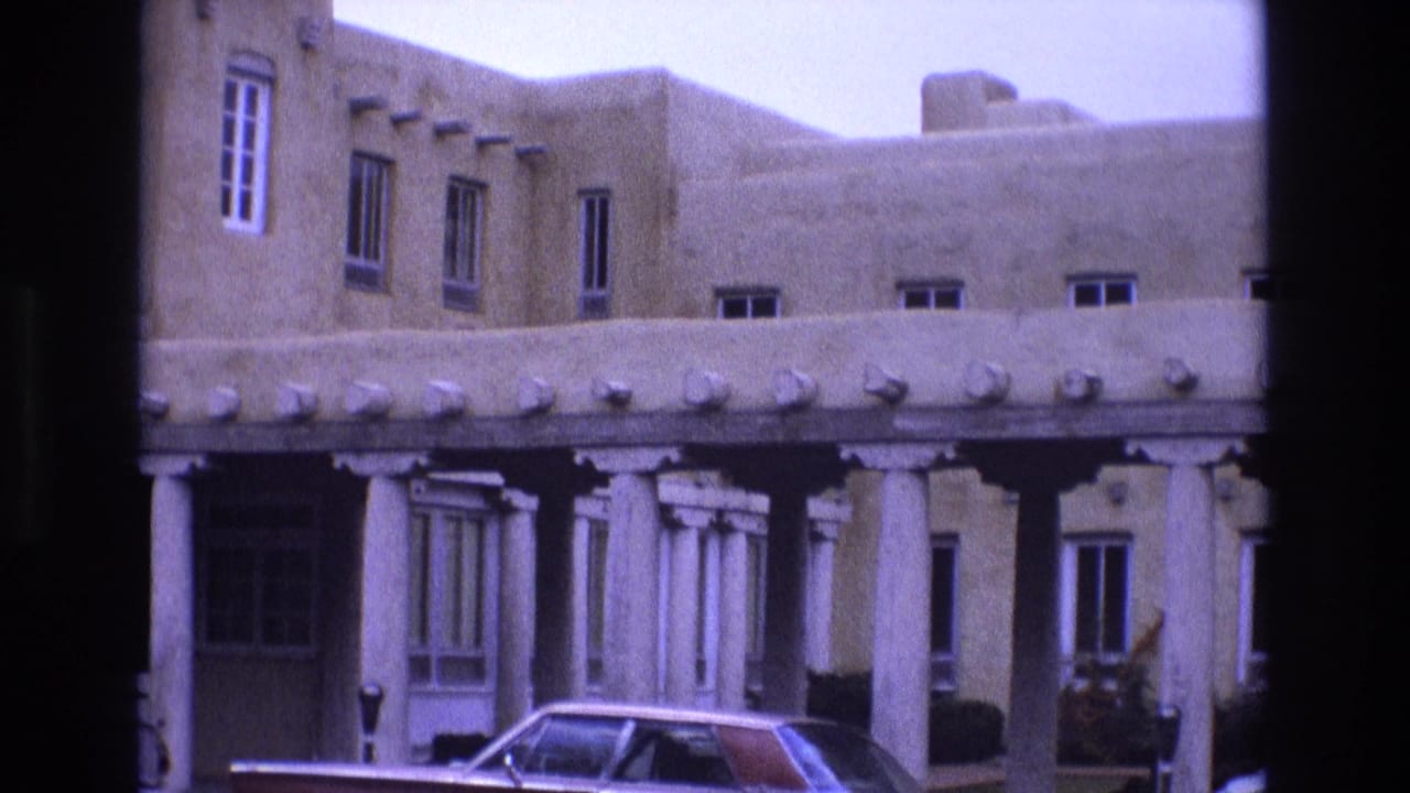 Adobe-style building facade with white columns and a parked car in front.